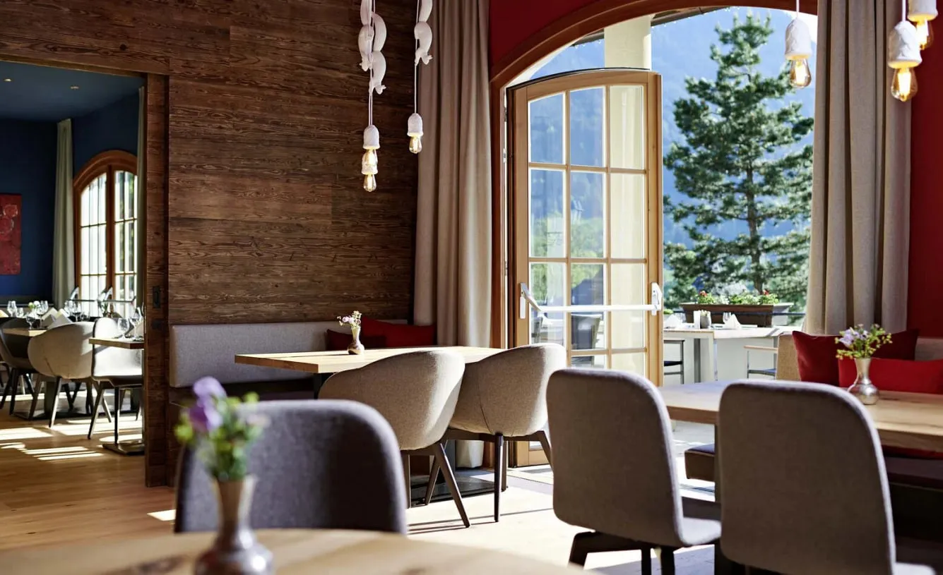 Restaurant des Schlosshotels Kitzbühel mit Holztischen und offener Tür zur Terrasse