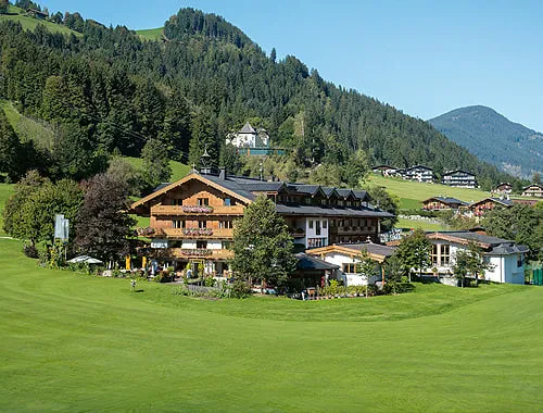 Hotel Rasmushof am Golfplatz, dahinter ein bewaldeter Berghang
