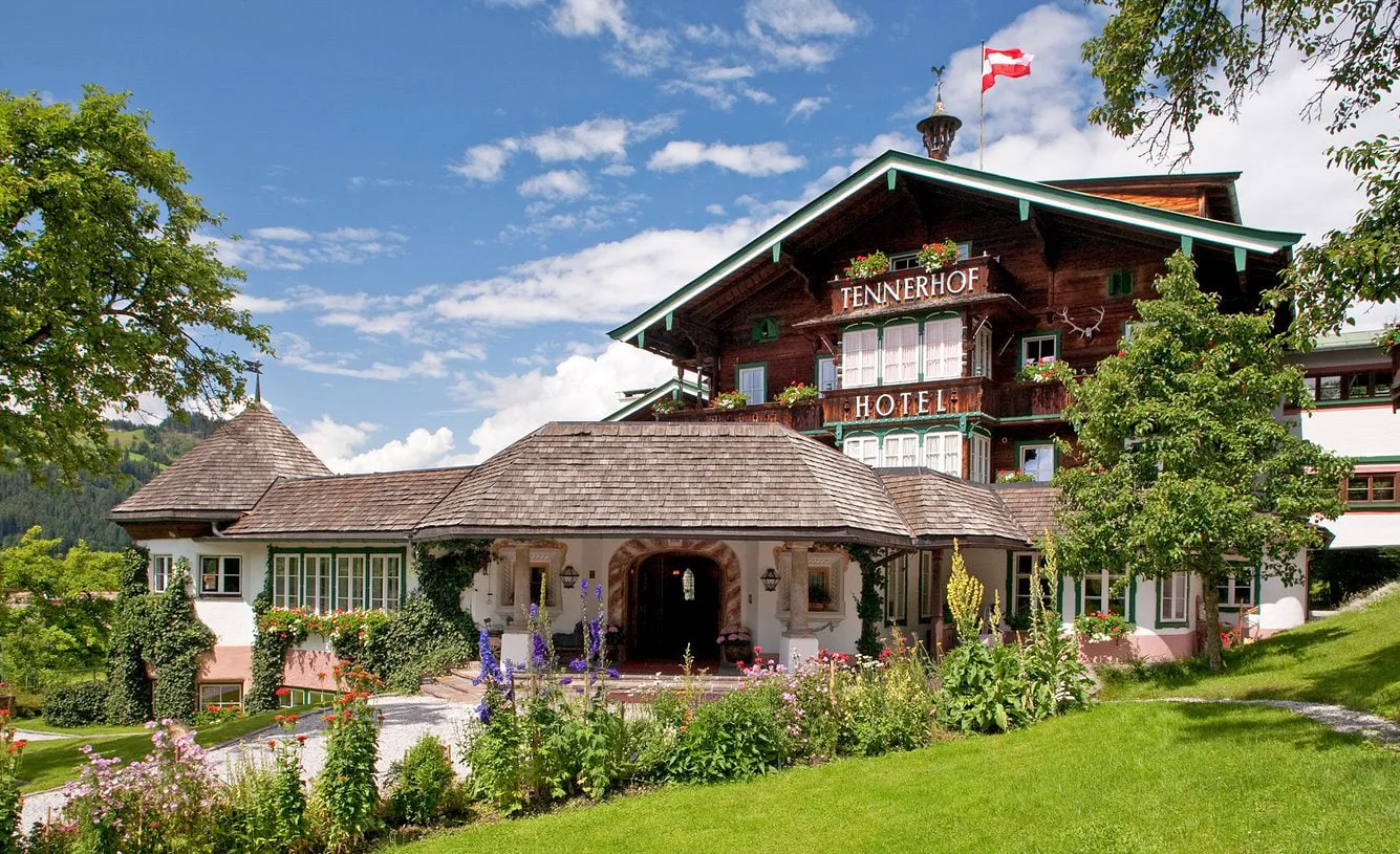 Hotel Tennerhof mit Holzfassade, Fahne und blühendem Garten