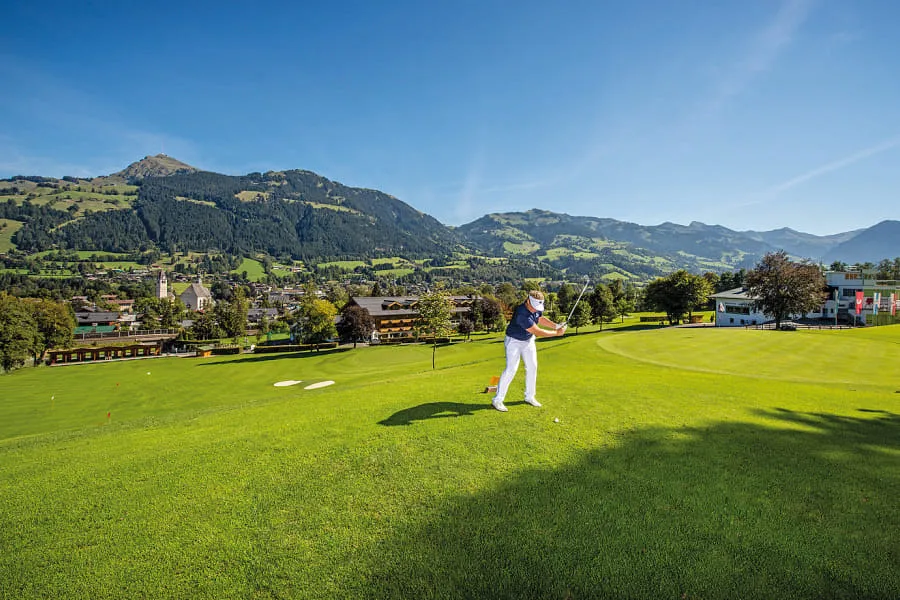 Golfer beim Abschlag auf dem Fairway, dahinter Kitzbühel
