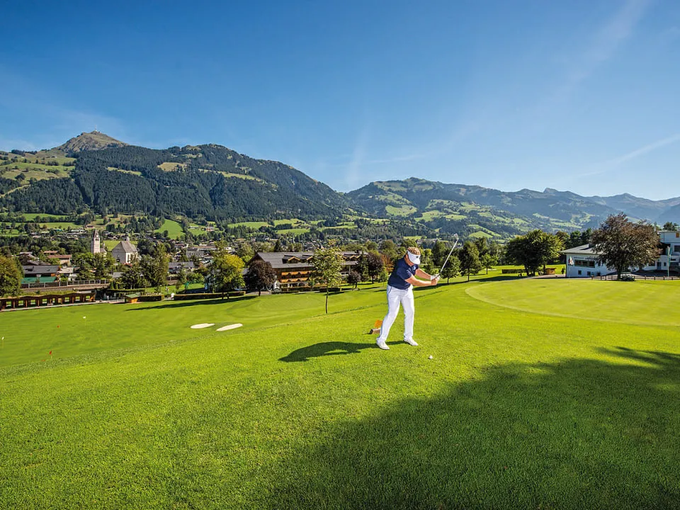 Golfer beim Abschlag auf dem Fairway, dahinter Kitzbühel